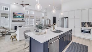 A modern kitchen with a central island, white cabinetry, stainless steel appliances, and pendant lighting. - Sandy Cheeks 409 COA (Port Aransas)