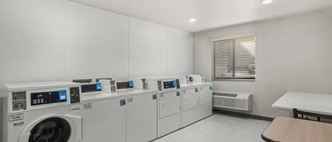 A laundry room with multiple washing machines, a table, and a window with blinds.