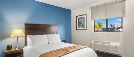 Habitación de hotel con cama, mesita de noche con lámpara, ventana con vistas al exterior y aire acondicionado de pared.