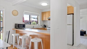 Eine moderne Küche mit Holzarbeitsplatte, weißen Barhocker, Mikrowelle, Herd und Kühlschrank.