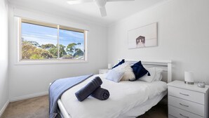 Ein Schlafzimmer mit Bett, Nachttisch, Fenster mit Blick auf Bäume und Deckenventilator.