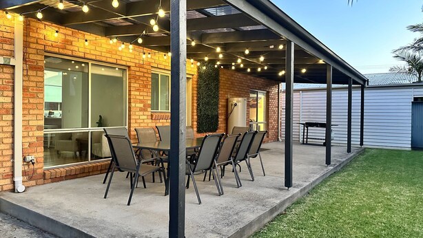 Ein überdachter Patio-Bereich mit Backsteinmauern, einem Tisch mit Stühlen und Lichterketten.