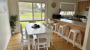 Eine moderne Küche mit Essbereich, ausgestattet mit einem großen Fenster, Holzboden und weißen Möbeln.