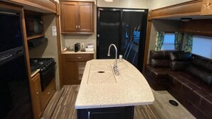 A compact RV kitchen with a granite countertop, stainless steel sink, and wooden cabinets. - Sunniland Ranch Airport 08FD Fly-In Destination

 (Okeechobee)