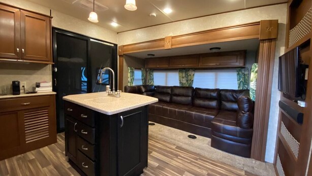 A compact RV kitchen with a central island, built-in cabinets, and a seating area with a brown leather couch. - Sunniland Ranch Airport 08FD Fly-In Destination

 (Okeechobee)