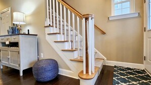 A staircase with white railings and wooden steps, a round blue ottoman, and a patterned rug on a wooden floor. - 4-bedroom vacation home steps to Seaside Heights Boardwalk (Seaside Heights)