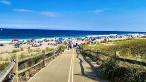 A wooden boardwalk leading to a beach with people and umbrellas. - 4-bedroom vacation home steps to Seaside Heights Boardwalk (Seaside Heights)