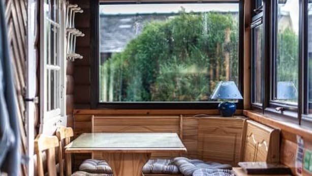Interior acogedor de una cabaña con un rincón de madera para sentarse, una mesita y un ventanal con vistas a la vegetación.