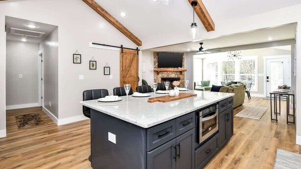 A modern kitchen with a large island, wooden beams, and a stone fireplace.