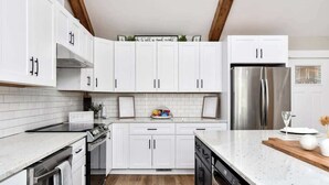 A modern kitchen with white cabinets, stainless steel appliances, and a wooden ceiling.