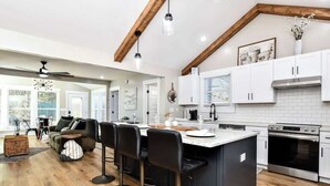 A modern kitchen with white cabinets, a central island with bar stools, a large oven, and a ceiling fan.