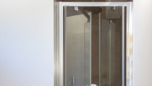 Ett modernt badrum med en dusch som är avskärmad med glasväggar, en vit vägg och ett beige golv.