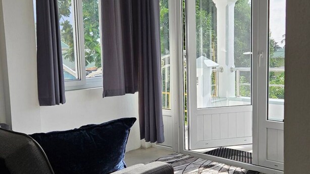 Ein modernes Wohnzimmer mit einer Couch, einem großen Fenster mit Vorhängen und Blick auf Grünflächen.