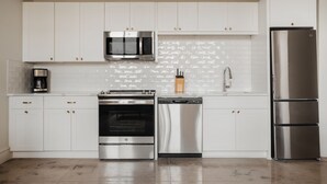A modern kitchen with white cabinets, stainless steel appliances, and a tiled backsplash.