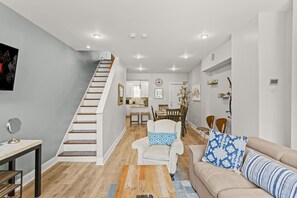 A modern living room with a staircase, a dining area, and a kitchen in the background. - Walk Everywhere, Comfortable Park-Front Escape w/ Free Parking! (Philadelphia)