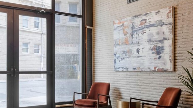 A lobby with a checkered floor, two leather chairs, a modern chandelier, and a large abstract painting on the wall.