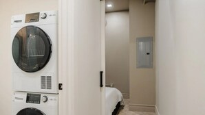 Une buanderie avec des machines à laver et des sèche-linge superposés, un lit dans la pièce adjacente et un interrupteur sur le mur.
