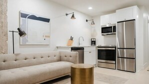 Une cuisine moderne avec des meubles blancs, des appareils en acier inoxydable et un canapé beige.