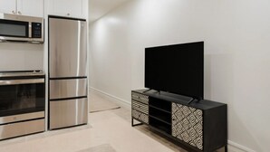 Una cocina moderna con electrodomésticos de acero inoxidable, un televisor de pantalla plana sobre un mueble negro y armarios blancos.