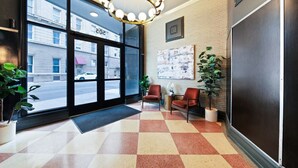 A hotel lobby with a checkered floor, two armchairs, a table, and a large window with a view of the street.