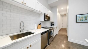 A modern kitchen with white cabinets, a stainless steel sink, a microwave, and an oven.