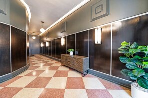 A hallway with a checkered floor, dark walls, and a wooden bench with a plant. - Historic Light, Modern Living at La Luz (San Antonio)
