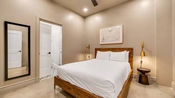 A bedroom with a wooden bed, a ceiling fan, a framed map on the wall, and a small round table with a lamp.
