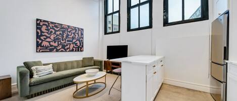 Ein modernes Wohnzimmer mit einer Couch, einem Couchtisch, einem Fernseher und einer Küchenzeile inklusive Kühlschrank und Schränken.