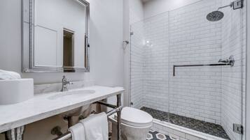 A modern bathroom with a white vanity, a large mirror, a glass shower enclosure, and a toilet.