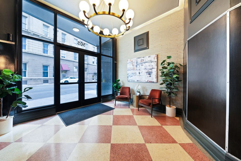 A hotel lobby with a checkered floor, two armchairs, a table, and a large window with a view of the street.