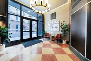 A hotel lobby with a checkered floor, two armchairs, a table, and a large window with a view of the street.