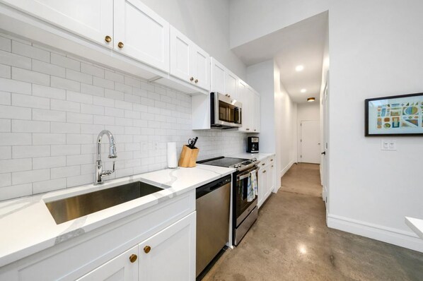 A modern kitchen with white cabinets, a stainless steel sink, a microwave, and an oven. - Historic Light, Modern Living at La Luz (San Antonio)