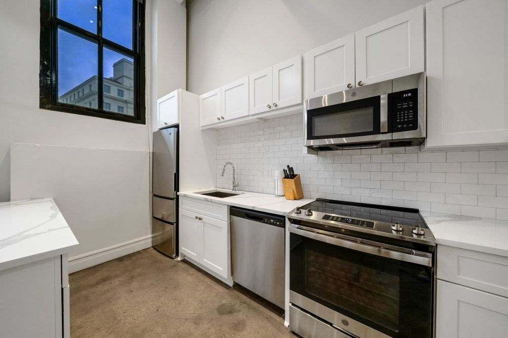 A modern kitchen with white cabinets, stainless steel appliances, and a window with a city view.