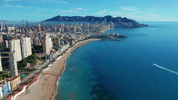 Un paysage urbain côtier avec de hauts immeubles, une plage et des montagnes en arrière-plan.