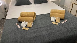 Un lit bien fait, avec deux serviettes, un flacon de lotion et un savon sur une couverture grise.