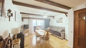 Un salon comprenant un canapé, une table à manger, des chaises, un téléviseur et un ventilateur de plafond.