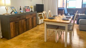 Une cuisine compacte avec un îlot central en bois, une table à manger pour quatre personnes et un téléviseur posé sur un meuble.