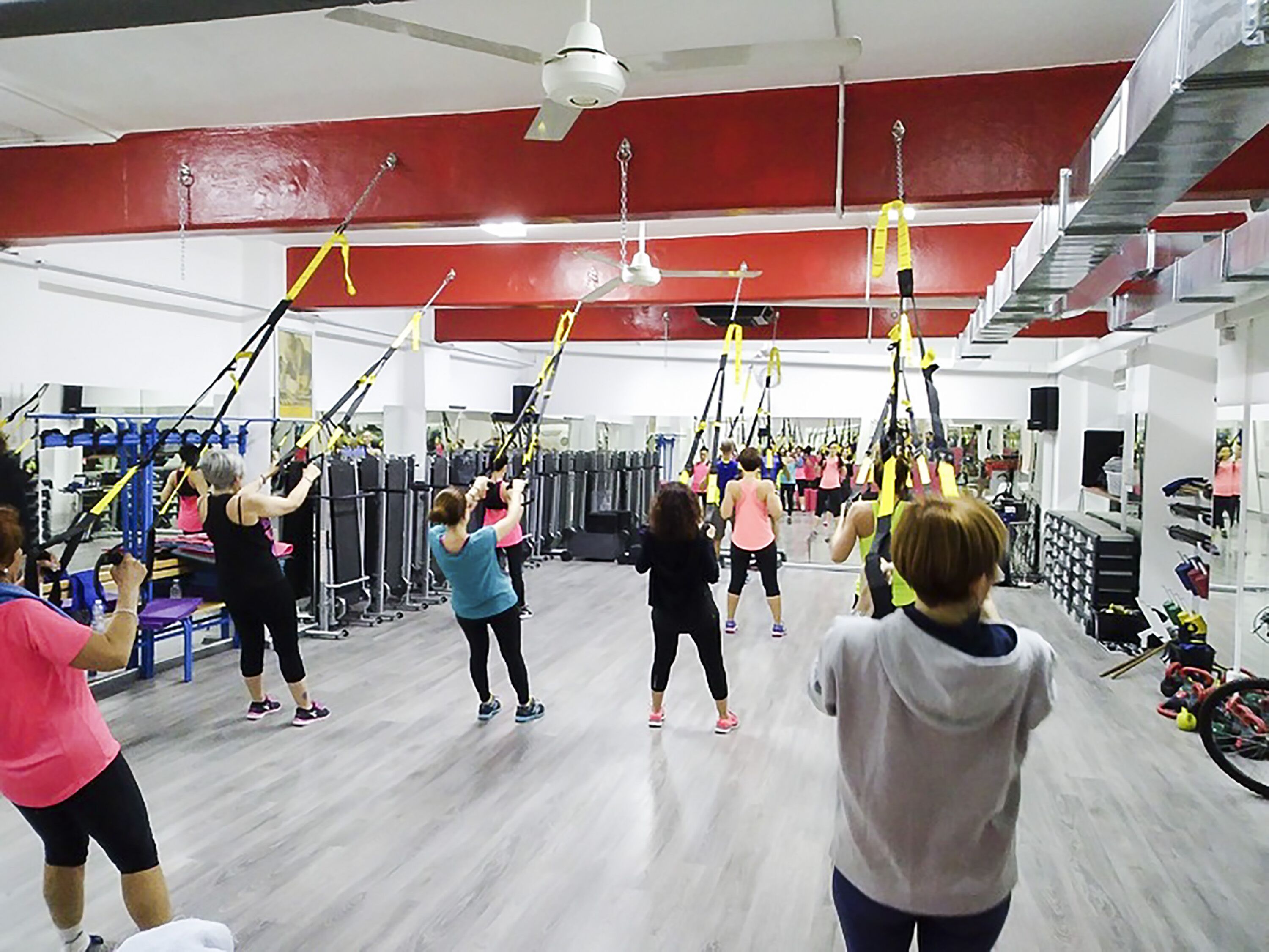 A group of people exercising with suspension straps in a gym with red walls and a high ceiling.