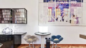 Une pièce moderne avec une bibliothèque noire, une table ronde et deux chaises, ainsi qu’une œuvre d’art murale.