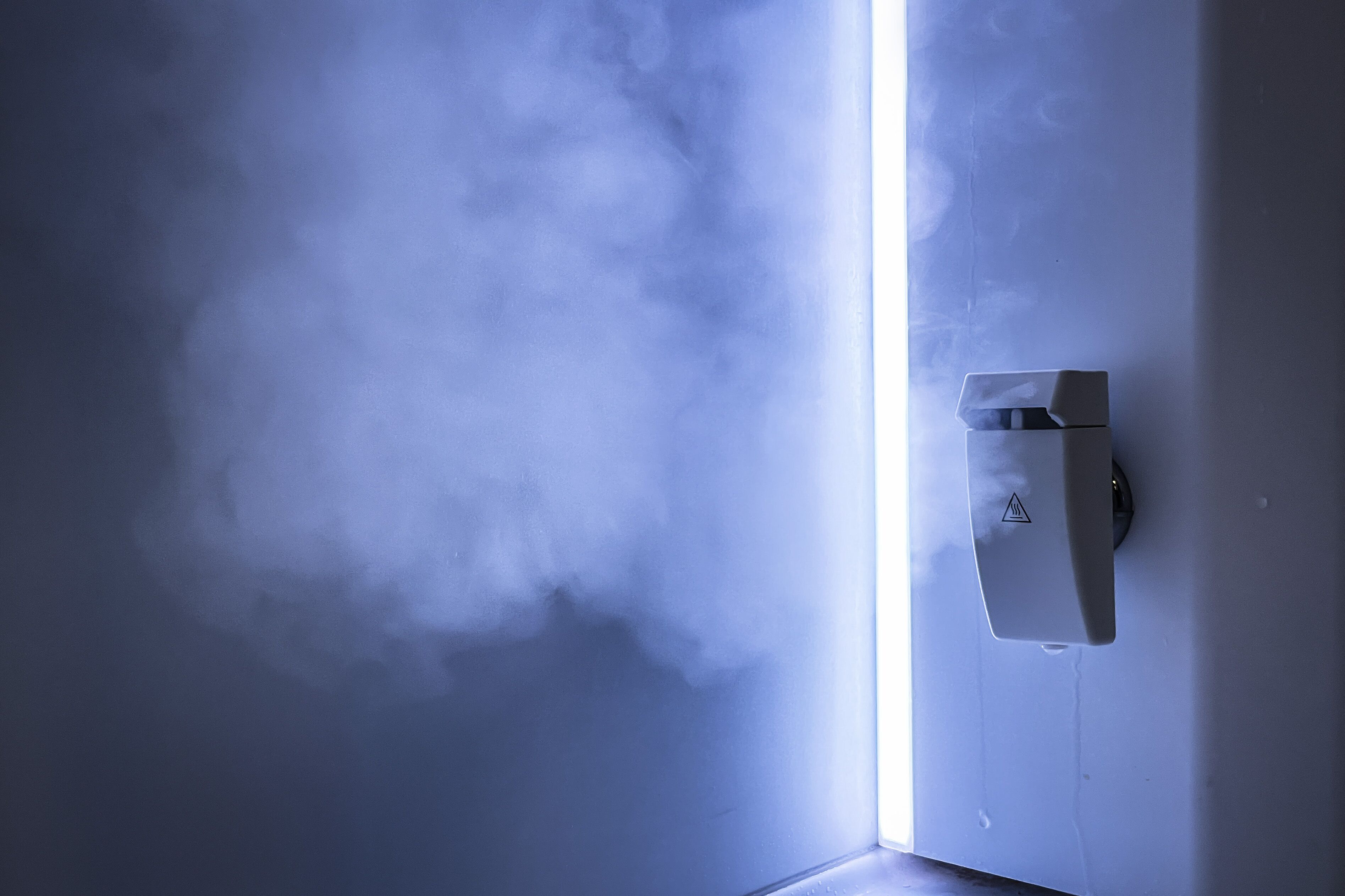 A bathroom with a steam shower, a safety warning sign, and a visible water leak.