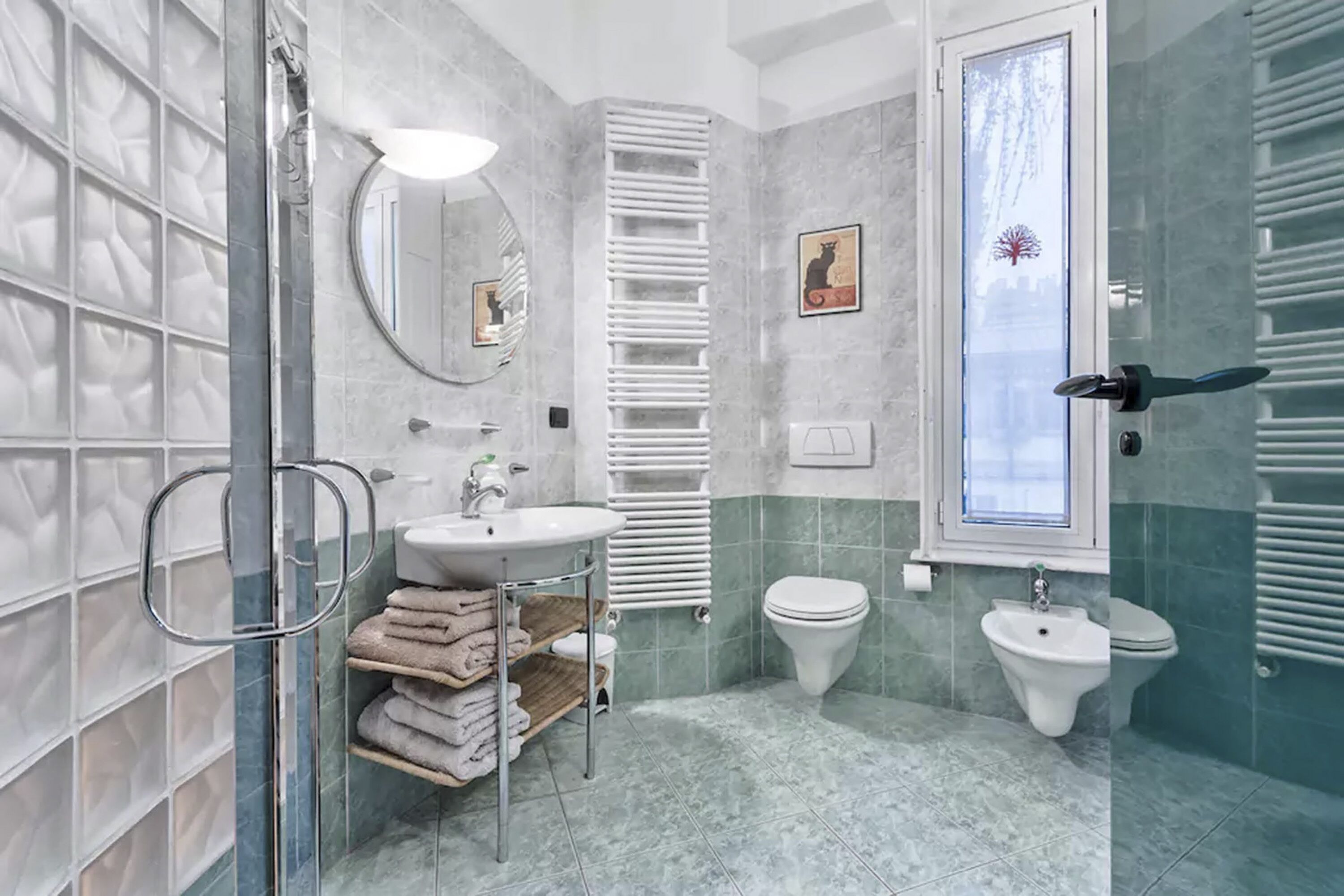 A modern bathroom with a glass shower enclosure, a white sink, a bidet, and a towel rack.