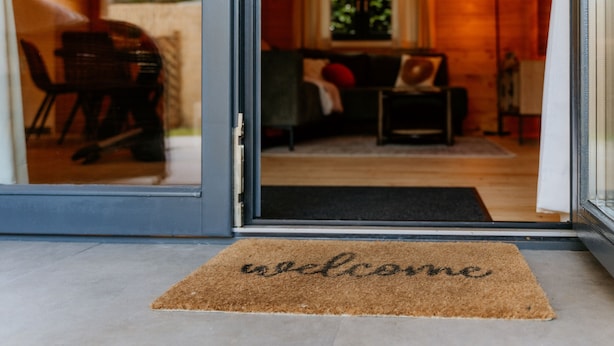 A doorway leading into a room with a sofa, a lamp, and a welcome mat.
