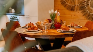 A dining table set with croissants, bread, and a fruit bowl.