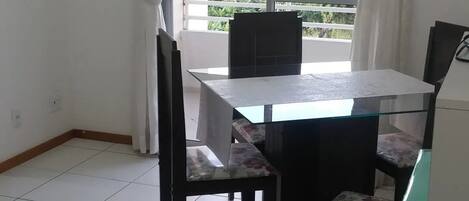 A room with a dining table, chairs, a TV, and a red ottoman.