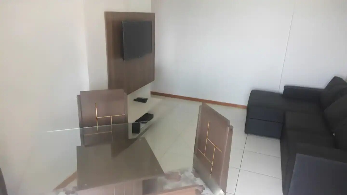 A living room with a flat-screen TV mounted on the wall, a dark-colored sofa, and a glass coffee table.
