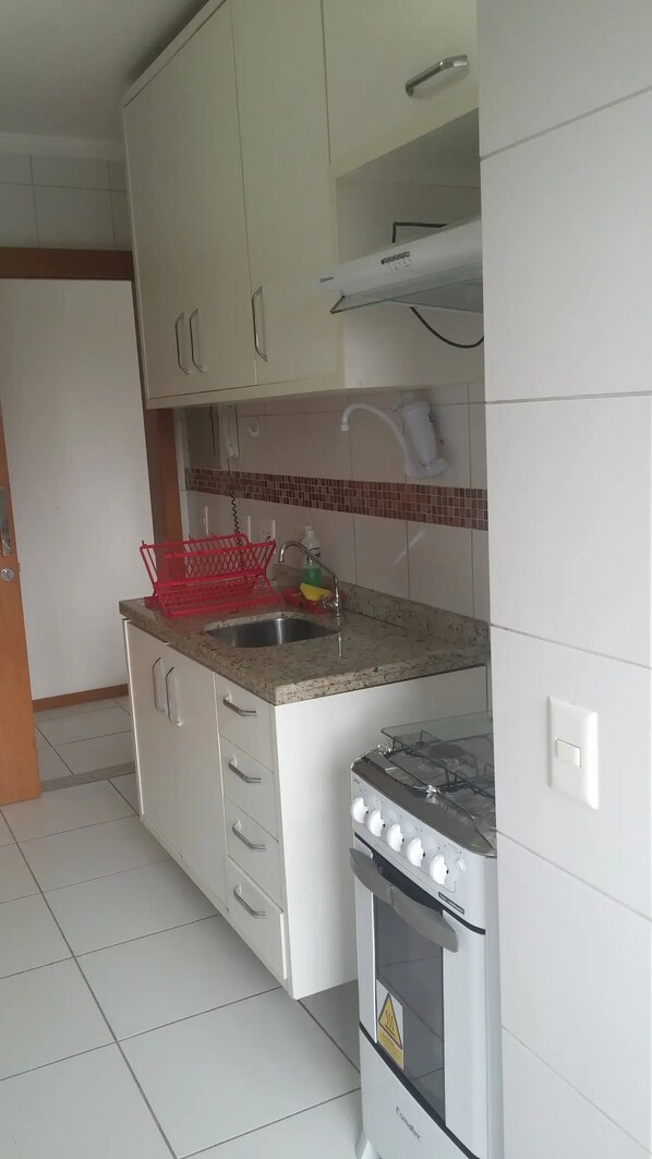 Una cocina con armarios blancos, un lavamanos de acero inoxidable, un escurreplatos rojo y una estufa a gas.