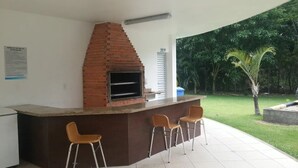 An outdoor kitchen area with a brick oven, two bar stools, and a counter. - A 300 Mtos da Arena da Amazônia e Centro de Convenções Vasco Vasquez (Chapada)