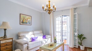 A living room with a sofa, a glass coffee table, a lamp, a painting, and a view through a window.