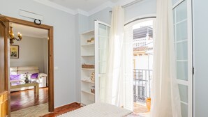 A bedroom with a bed, a wardrobe, a mirror, a sofa, and a view of the outside balcony.