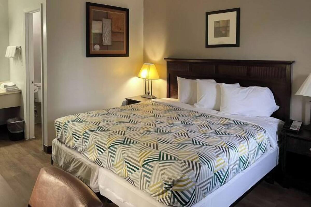 Ein Hotelzimmer mit einem Bett, einem Nachttisch, einer Lampe, einem Sessel und einer Tür zu einem Badezimmer.